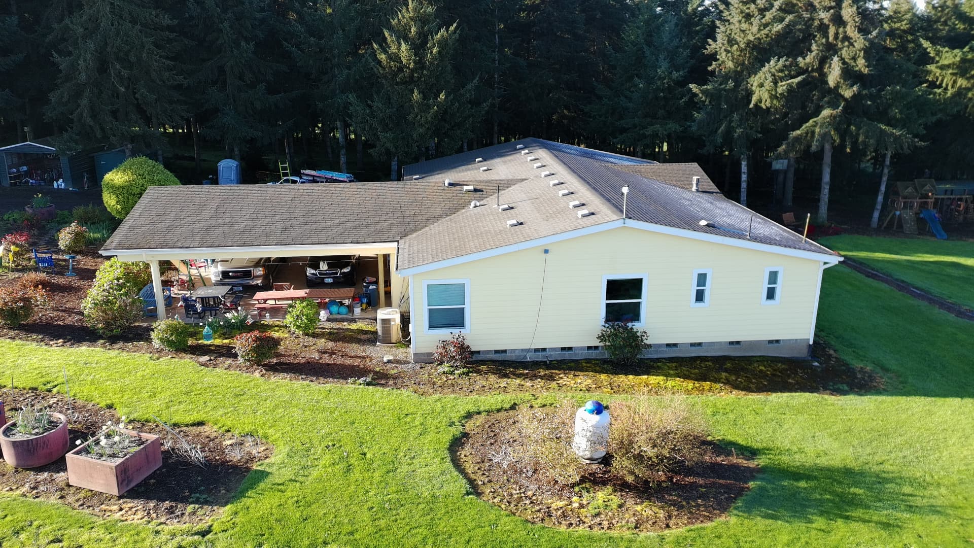 Completed roof on a single-story yellow home bordered by tall fir trees