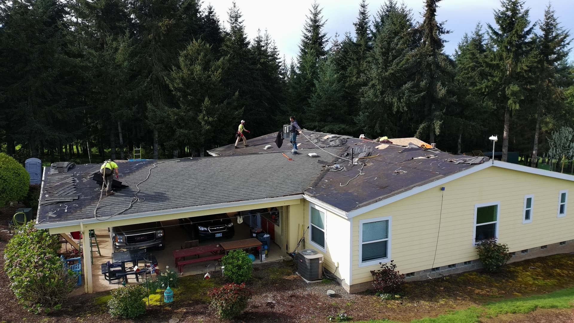 Roofing crew removing old shingles from a ranch-style home with a carport