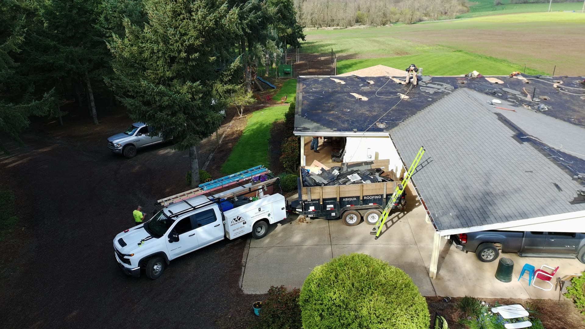 Abiqua Roofing service truck and dump trailer parked at a rural job site during a roof tear-off